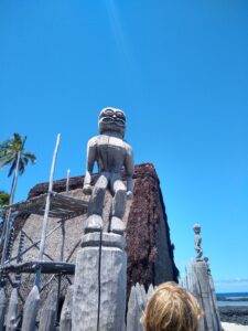 A wooden tiki statue in front of a temple made of ferns and leaves